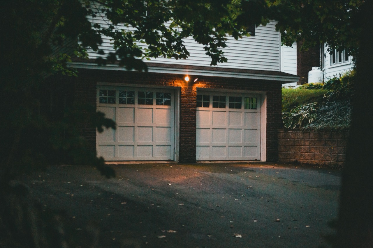 A two-car residential garage with paneled doors at dusk, porch light on