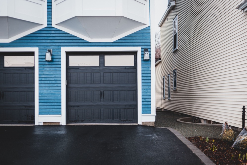 A coastal clapboard home with a dark carriage-style garage door on a wet driveway